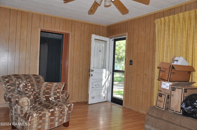 sitting room featuring light hardwood / wood-style floors, wooden walls, and ceiling fan