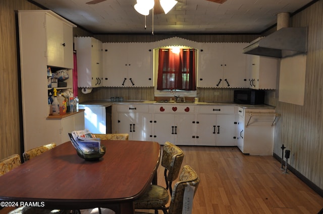 kitchen featuring wall chimney range hood, light wood-type flooring, white cabinets, sink, and ceiling fan