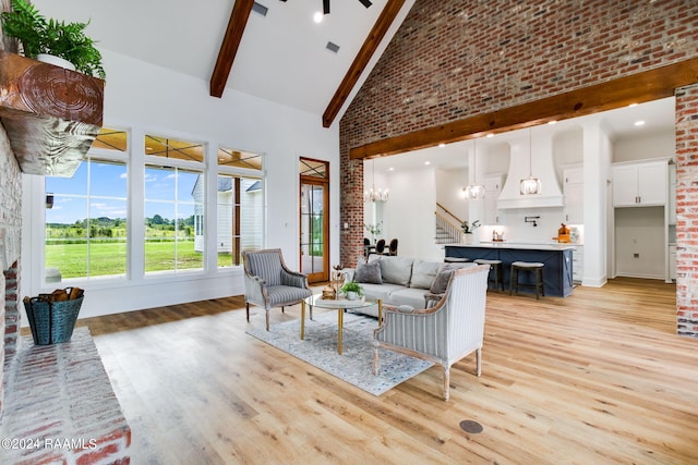 living room featuring beam ceiling, high vaulted ceiling, light hardwood / wood-style floors, and an inviting chandelier