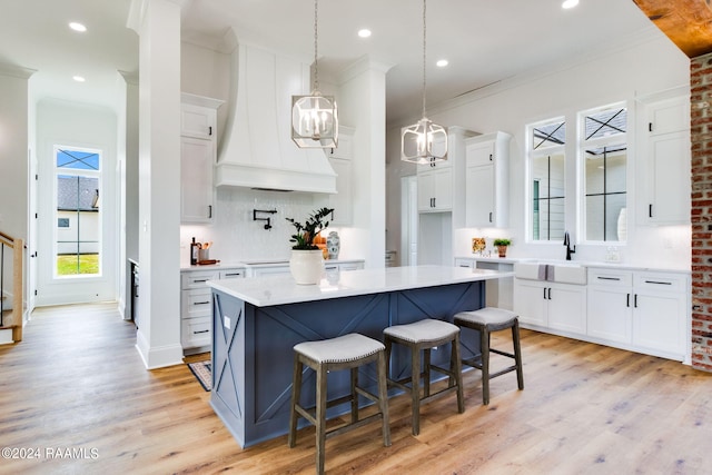 kitchen featuring light hardwood / wood-style floors, white cabinetry, a kitchen island, premium range hood, and tasteful backsplash