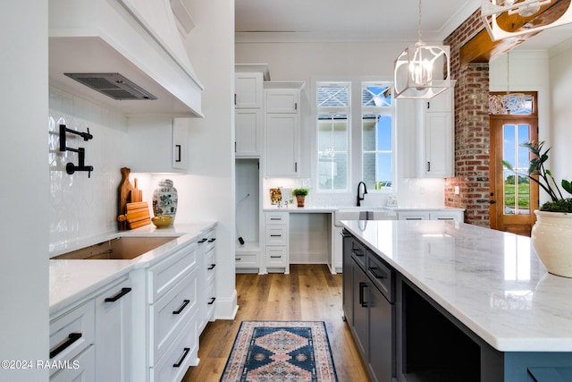 kitchen featuring decorative light fixtures, light hardwood / wood-style floors, crown molding, white cabinetry, and light stone countertops