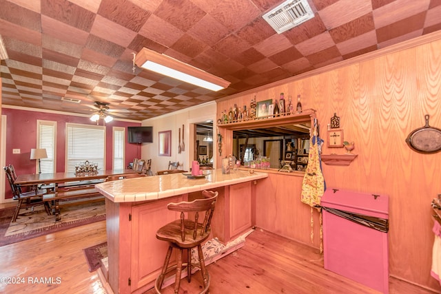 kitchen featuring tile countertops, a kitchen breakfast bar, ceiling fan, light hardwood / wood-style floors, and kitchen peninsula