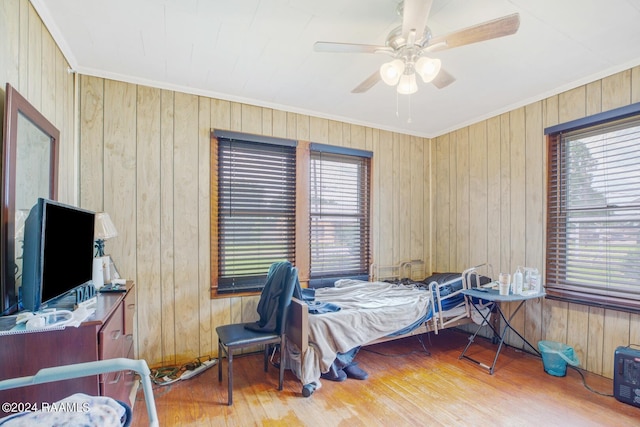 bedroom featuring wooden walls, hardwood / wood-style flooring, ceiling fan, and ornamental molding