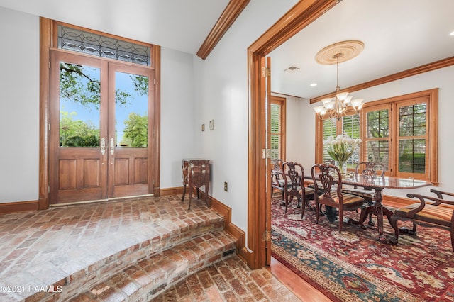 entryway with crown molding, french doors, and an inviting chandelier