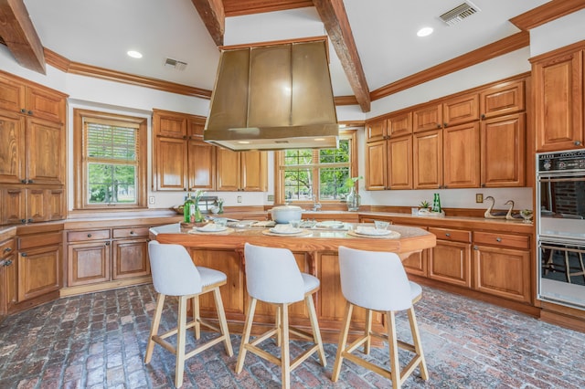 kitchen with island range hood, beam ceiling, a healthy amount of sunlight, and a breakfast bar area