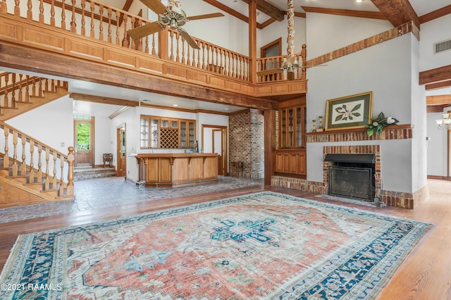 living room featuring wood-type flooring, a towering ceiling, ceiling fan, and a brick fireplace