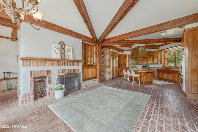 living room featuring brick wall, lofted ceiling with beams, a brick fireplace, a notable chandelier, and sink