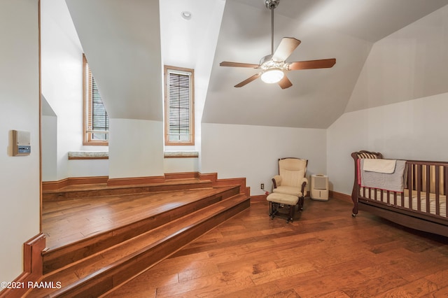 bedroom with a nursery area, ceiling fan, vaulted ceiling, and hardwood / wood-style floors