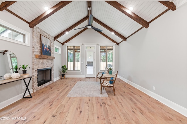 sitting room with beam ceiling, ceiling fan, a stone fireplace, high vaulted ceiling, and light wood-type flooring