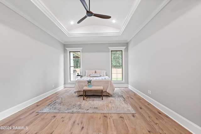 bedroom with light wood-type flooring, a raised ceiling, ceiling fan, and crown molding