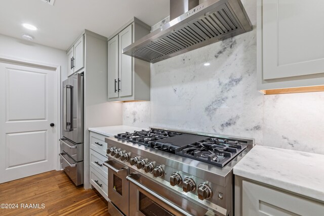 kitchen with light hardwood / wood-style flooring, tasteful backsplash, light stone counters, premium appliances, and wall chimney exhaust hood