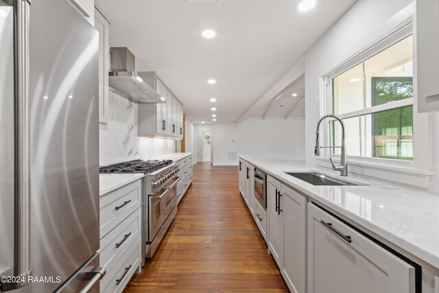 kitchen with a healthy amount of sunlight, tasteful backsplash, hardwood / wood-style floors, wall chimney exhaust hood, and appliances with stainless steel finishes