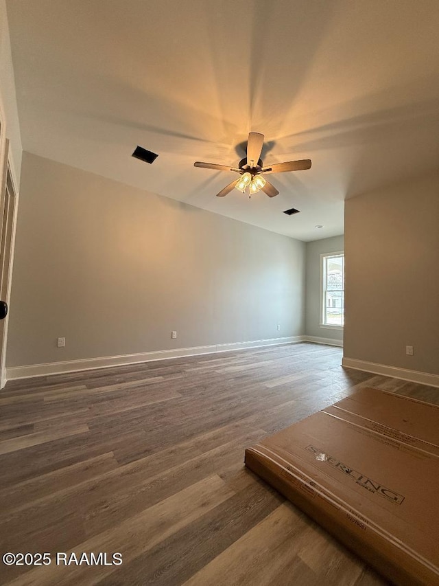 unfurnished room with a ceiling fan, visible vents, baseboards, and wood finished floors