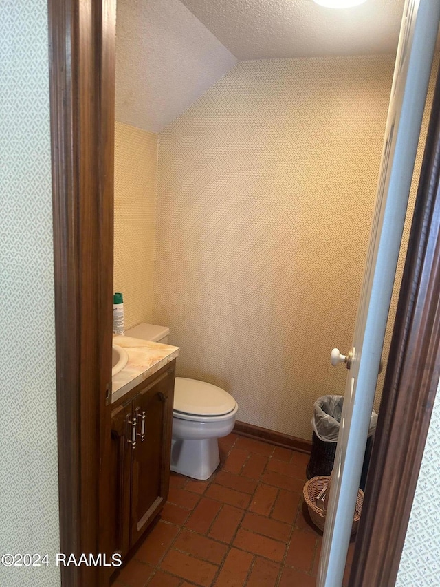 bathroom featuring a textured ceiling, lofted ceiling, tile flooring, vanity, and toilet