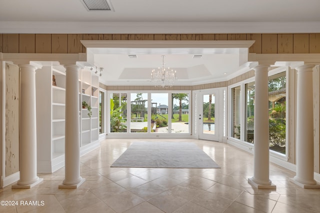 interior space with a tray ceiling, an inviting chandelier, ornamental molding, and light tile patterned flooring