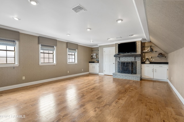 unfurnished living room featuring light hardwood / wood-style floors, lofted ceiling, crown molding, and a brick fireplace