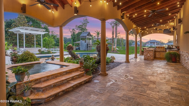 patio terrace at dusk with ceiling fan and exterior kitchen