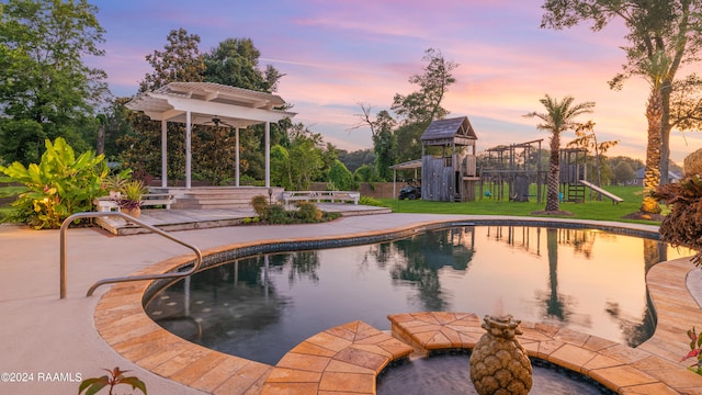 pool at dusk featuring a playground, a wooden deck, and a patio