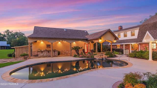 pool at dusk with a patio and area for grilling