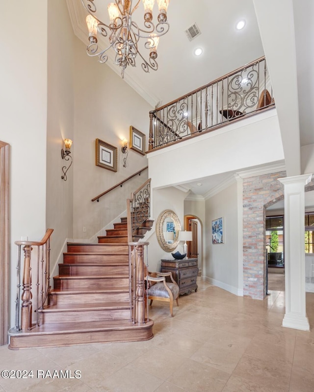 staircase featuring ornate columns, ornamental molding, a towering ceiling, and an inviting chandelier