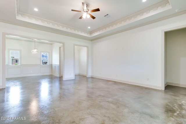 spare room with a raised ceiling, ceiling fan, concrete flooring, and ornamental molding