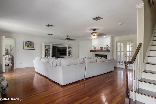 living room featuring french doors, a fireplace, ceiling fan, dark wood-type flooring, and brick wall