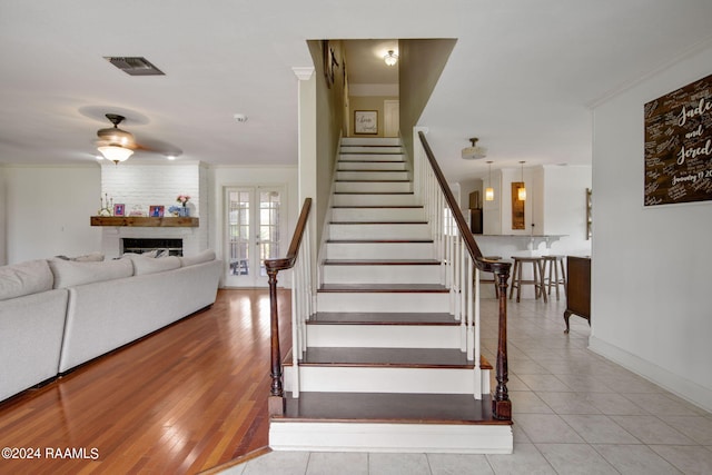 stairway with crown molding, wood-type flooring, a large fireplace, ceiling fan, and french doors