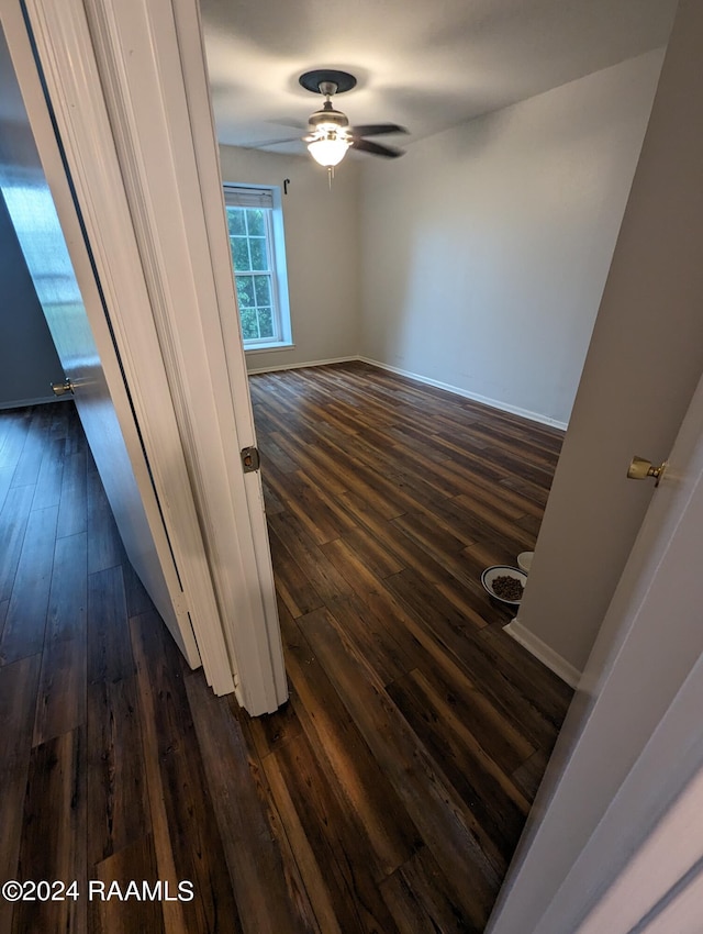 interior space with baseboards, a ceiling fan, and dark wood-style flooring