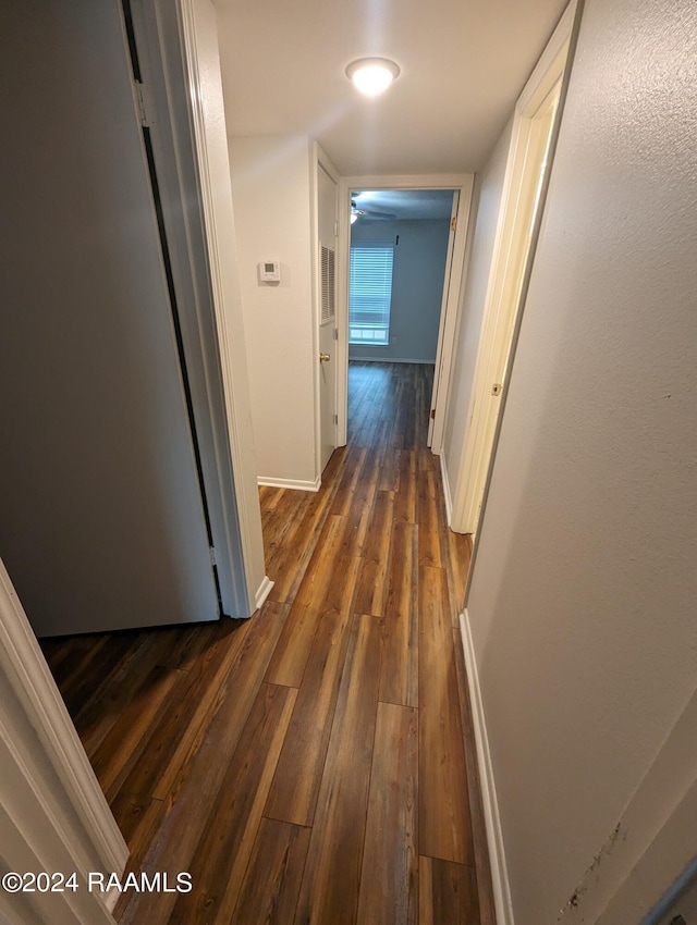 hall with dark wood finished floors, visible vents, and baseboards