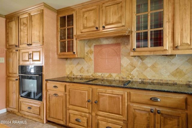 kitchen with black oven, decorative backsplash, light tile patterned floors, and dark stone counters