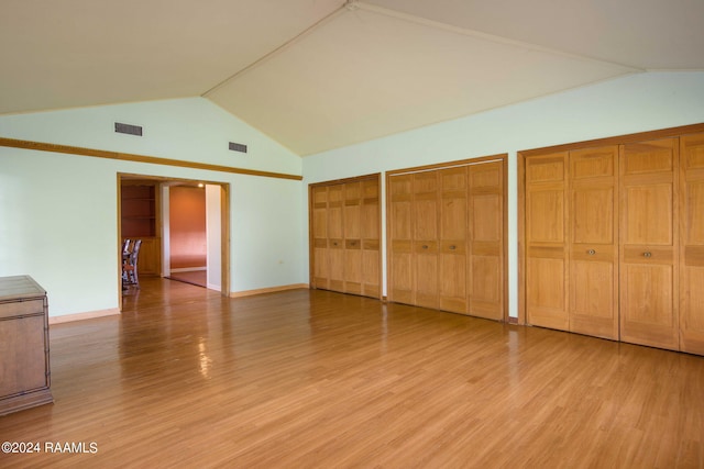 unfurnished bedroom featuring lofted ceiling, light wood-type flooring, and two closets