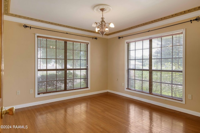 unfurnished room with hardwood / wood-style flooring, a healthy amount of sunlight, crown molding, and an inviting chandelier