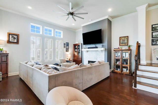 living room with a stone fireplace, crown molding, ceiling fan, and dark wood-type flooring