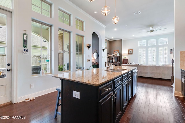 kitchen featuring a kitchen island with sink, sink, dark hardwood / wood-style floors, decorative light fixtures, and a breakfast bar area