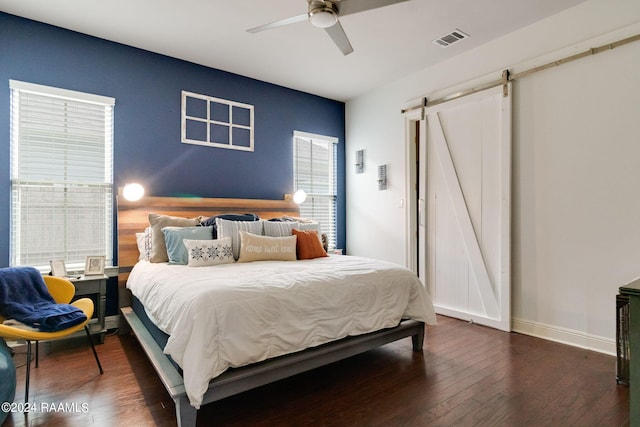 bedroom with dark hardwood / wood-style floors, a barn door, and ceiling fan