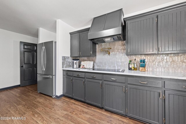 kitchen with dark wood-type flooring, wall chimney range hood, stainless steel fridge, black electric cooktop, and gray cabinets