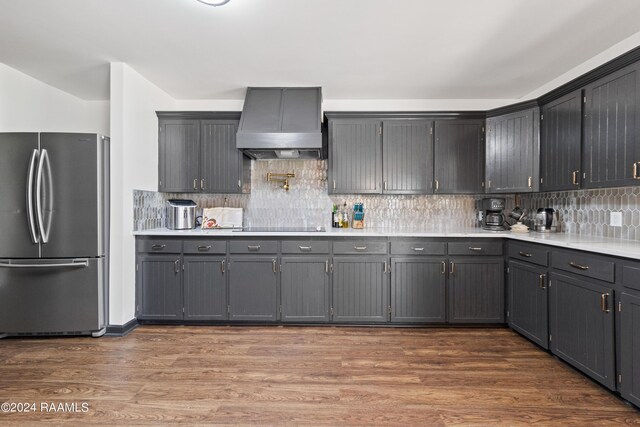 kitchen featuring wall chimney exhaust hood, dark hardwood / wood-style floors, backsplash, stainless steel fridge, and black electric stovetop