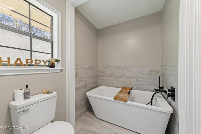 bathroom with a washtub, toilet, and tile walls