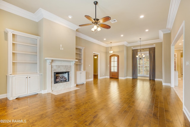 unfurnished living room with hardwood / wood-style floors, ceiling fan with notable chandelier, a fireplace, crown molding, and built in shelves