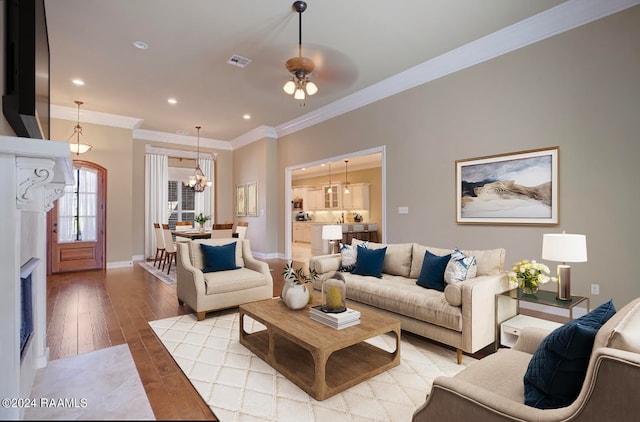 living room with ceiling fan with notable chandelier, light hardwood / wood-style floors, and ornamental molding