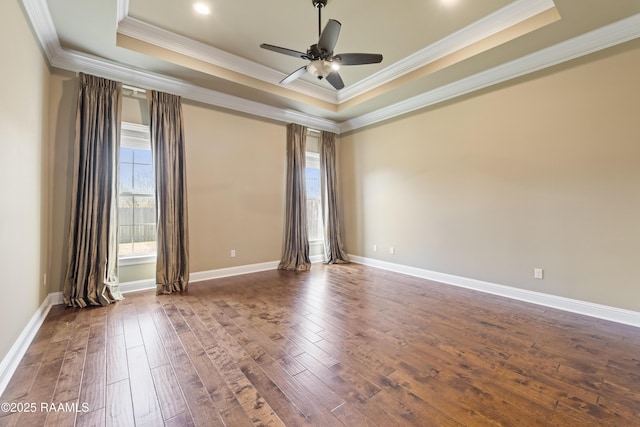 empty room featuring a tray ceiling, dark wood-type flooring, and baseboards