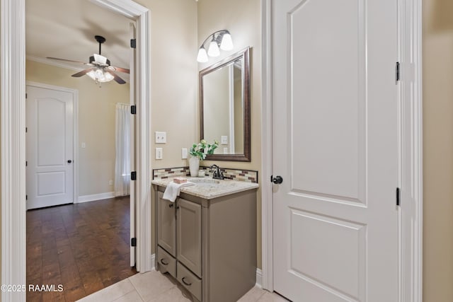 bathroom with baseboards, ceiling fan, ornamental molding, wood finished floors, and vanity