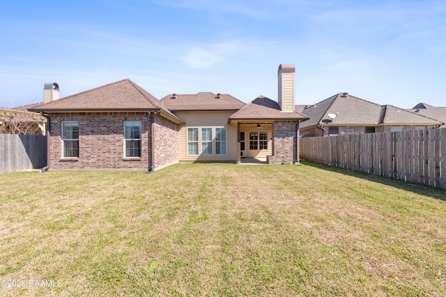 rear view of house with a yard, a chimney, and a fenced backyard