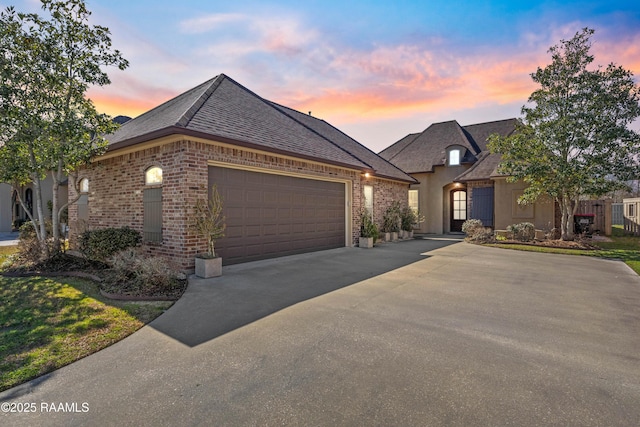 french country home with an attached garage, brick siding, a shingled roof, driveway, and stucco siding