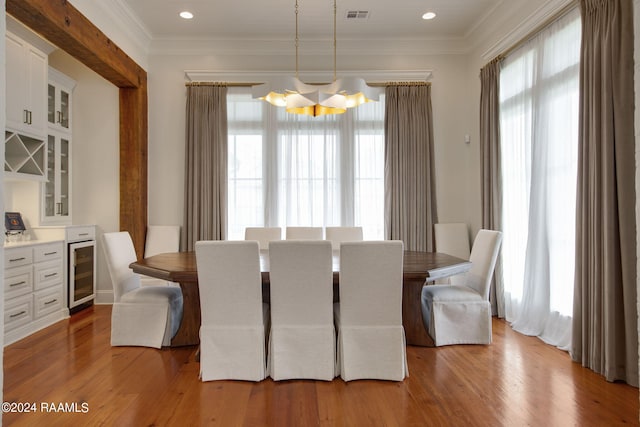 dining area with light wood-type flooring, crown molding, and wine cooler