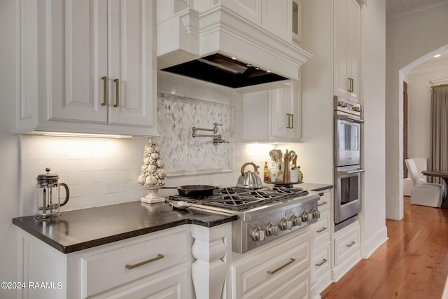 kitchen featuring light wood-type flooring, premium range hood, ornamental molding, stainless steel appliances, and white cabinets