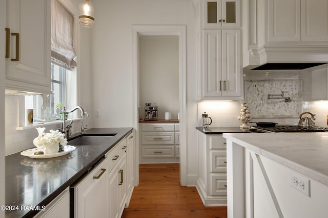 kitchen featuring sink, dark stone countertops, decorative backsplash, white cabinets, and light wood-type flooring