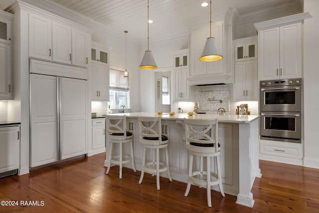 kitchen with pendant lighting, dark wood-type flooring, stainless steel double oven, an island with sink, and white cabinetry