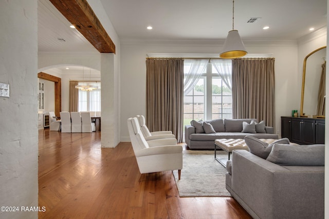 living room featuring beamed ceiling, hardwood / wood-style flooring, crown molding, and a notable chandelier