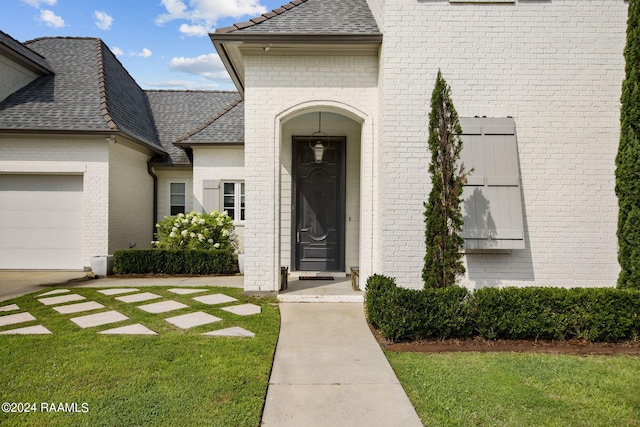 view of exterior entry featuring a lawn and a garage